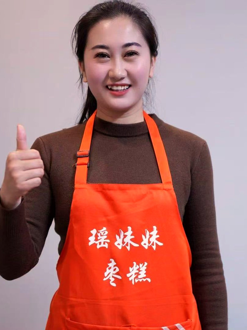瑶妹妹身穿印有「瑶妹妹枣糕」的橙色围裙,竖起大拇指